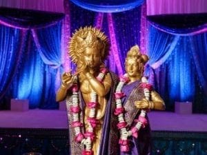 Behold the majestic scene where two golden guardians rise, draped in radiant flower garlands, each standing sentinel before a tapestry of azure and amethyst. This opulent realm is tailor-made for immortalizing moments of joy and grandeur. It provides an ideal backdrop for the legendary Michigan Wedding DJ or Event Heroes’ epic photo booth rental, enhancing any celebration with its timeless elegance. :The Event Heroes at Black Tie Productions