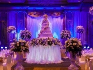 In the grand hall of celebration, where dreams took flight, rose a mighty multi-tiered cake of grandeur, encircled by vibrant battalions of blooming floral wonders. Enhanced by mesmerizing purple illumination that rippled through the air like mystical energy waves, the scene was set for an epic union. Event Heroes swooped in with their legendary photo booth powers, wielding cameras like enchanted shields to immortalize memories and ensure every guest left with a token from this unforgettable realm. :The Event Heroes at Black Tie Productions