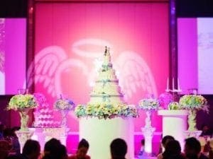 In the heart of a grand celebration, amidst the backdrop of love and unity, stands the majestic wedding cake—a tower of elegance gracing its pedestal like a beacon of hope and sweetness. Encircled by an army of exquisite floral guardians and bathed in an ethereal pink glow, this cake transforms into a symbol of everlasting romance. Behind the scenes, it’s Event Heroes who orchestrate this symphony of joy; their superpower is precision coordination. In tandem with Michigan’s legendary DJ maestro, they weave magic into every moment, ensuring this celebration is nothing short of legendary. :The Event Heroes at Black Tie Productions