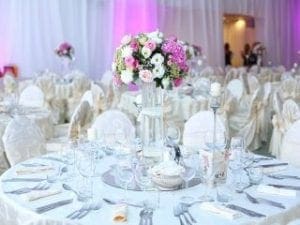 In a world where elegance meets enchantment, behold the magnificent wedding reception! Picture round tables adorned with pristine white tablecloths, transforming the venue into a bastion of grace. Enchanting floral centerpieces rise like vibrant beacons in the night. Behold, plates, glasses, and cutlery arranged with precision more meticulous than a superheros battle plan, all bathed in an ethereal glow of soft pink light that whispers romance. But wait—there’s more to this tale! Unleash unparalleled joy by summoning the power of a photo booth rental. Capture memories that will endure beyond time itself. This is no ordinary celebration; its an odyssey of love and elegance destined to shine forever!. :The Event Heroes at Black Tie Productions