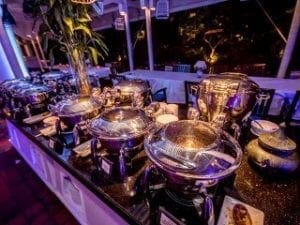 Behold the majestic buffet table, a realm of culinary treasures cloaked in shimmering covers, basking under the glowing ambiance of event lights. Here, amidst this splendid gathering, guests are invited to immortalize their legendary moments with the photo booth conjured by none other than Black Tie Productions—a true ally in creating timeless memories!. :The Event Heroes at Black Tie Productions