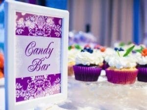 In a world where sweetness reigns supreme, the mighty emblem of Candy Bar towers above a battalion of cupcakes, each crowned with white frosting and shimmering berries, ready to unleash a symphony of flavors at this grand celebration! But no superhero event is complete without the exhilarating beats and electrifying vibes brought by an expert Michigan wedding DJ. With pulsating rhythms and dazzling event lighting, youll forge an atmosphere so powerful it transforms any gathering into an unforgettable epic of delight! Assemble your taste buds and prepare for a legendary encounter with pure sweetness!. :The Event Heroes at Black Tie Productions