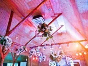 Behold, the Arched Haven of Triumph! Hanging high above, a valiant, decorated wooden ceiling boasts intricate floral formations and dazzling streams of light. These luminous strands dance like celestial constellations, crafting an atmosphere that enhances any heroic gathering with its enchanting radiance!. :The Event Heroes at Black Tie Productions