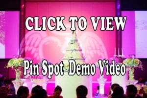 Behold! A majestic wedding cake rises like a citadel of sweetness, crowned by a celestial array of angelic wings and floral flourishes. Bathed in the radiant glow of heroic event lighting, this scene is as epic as love itself. An electrifying text overlay appears: CLICK TO VIEW Pin Spot Demo Video. Dare to imagine adding the sonic mastery of a Michigan wedding DJ or capturing memories with an iconic photo booth rental to transform your celebration into an unforgettable saga!. :The Event Heroes at Black Tie Productions