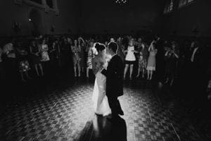 In the shadowy glow of a ballroom draped in shimmering lights, our heroic duo, the Bride-Wonder and Groom-Man, take to the dance floor for their first epic dance. As they gracefully glide and twirl to their own love ballad, an ensemble of captivated onlookers—assembled as their League of Guests—witness this legendary moment unfold. Like silent sentinels armed with cameras, they capture every fleeting second for posterity. And lo! A photo booth stands ready—a beacon of memory preservation—to ensure that every sidekick and citizen present can carve out their own piece of this unforgettable celebration!. :The Event Heroes at Black Tie Productions