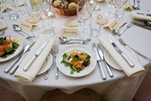 In the dazzling realm of dine-time heroics, an elegant dinner setting emerges like a majestic force. Plates of verdant salad appear as vibrant shields of health, flanked by gleaming cutlery forged from the finest metals. Crystal wine glasses stand ready, shimmering with heroic potential, while a sturdy breadbasket offers sustenance for the journey ahead. Secret identity name cards await discovery upon a pristine white tablecloth that stretches like an immaculate landscape. Black Tie Productions casts their luminous powers over the scene, enveloping it in a sophisticated glow that uplifts all who gather here. With an atmosphere charged with the energy of elegance and grace, this occasion becomes not just a meal but an epic gathering worthy of legends!. :The Event Heroes at Black Tie Productions