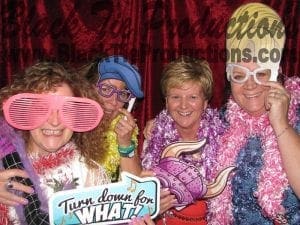 *In the vibrant realm of celebration, four daring individuals don costumes of vivid hues, oversized spectacles, and flowing feathered capes. They strike a heroic pose alongside their emblematic banner proclaiming, Turn down for what? against a backdrop as bold as their spirit. In the quest to capture these electrifying moments for your gathering, summon the forces of Black Tie Productions’ photo booth rental—a powerful ally providing instant price quotes to supercharge your events.*. :The Event Heroes at Black Tie Productions