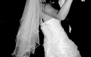 In a world where love conquers all, the Bride and Groom stand as majestic heroes of their own tale. Under the radiant glow of event lighting, they embark on their first dance—a graceful waltz that transcends time. She wears her armor: a veil cascading from her brow and a strapless gown that flows with elegance and power. Beside her stands the Groom, sharp in his tailored suit, exuding confidence as he joins his partner in this synchronized expression of unity. Captured by Black Tie Productions, this striking black-and-white photograph immortalizes their perfect moment—a testament to their unbreakable bond and fearless love. :The Event Heroes at Black Tie Productions