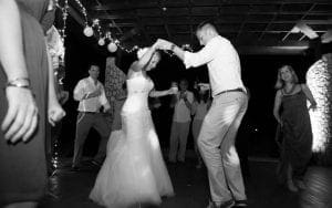 Amidst the shimmering strings of light that hung like celestial stars above, our dynamic duo – the Bride and Groom – took to the dance floor like legendary heroes stepping into destiny. Their movements were fluid and powerful, a symphony of grace on a wooden stage suspended between reality and dreams. As they twirled with effortless elegance, their admiring guests encircled them, witnesses to this extraordinary display of loves power. The atmosphere was charged with an enchanting energy, masterfully crafted by the illustrious Black Tie Productions, transforming this unforgettable night into something truly magical. :The Event Heroes at Black Tie Productions