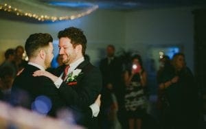 Under the sparkling canopy of string lights, two dashing gentlemen, dressed in their finest suits, glide gracefully across the dance floor. They move in perfect harmony, each step charged with the electricity of a thousand dreams. One of them clutches a bouquet as if it contains all the power in the universe. Around them, guests watch with eyes aglow, captivated by their elegant choreography. In this moment frozen by time and captured effortlessly by a photographers lens, magic fills the air. Its clear that Event Heroes have orchestrated yet another heart-stopping spectacle. With powers beyond ordinary comprehension—like deploying enchanted photo booths—they elevate any gathering into an adventure worthy of legend. Let Event Heroes transform your next event into an unforgettable saga with their extraordinary services; your memories will thank you for it!. :The Event Heroes at Black Tie Productions