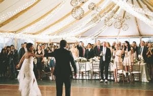 In the heart of Michigan, beneath a billowing tent that serves as their fortress of love, our heroic couple sways elegantly to the rhythm of destiny. Bathed in the luminescent glow of twinkling string lights—like stars summoned by cosmic power—they captivate an audience of finely dressed allies who watch with beaming admiration. The air pulses with a magical ambiance, crafted by a DJ whose turntables spin tales as grand as any legendary saga. Here, amidst this union and reverence, they dance not just for each other, but for all those who believe in the power of true love’s triumph!. :The Event Heroes at Black Tie Productions