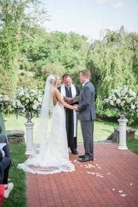 Under the golden glow of an outdoor paradise, where natures beauty forms a perfect backdrop, our courageous couple awaits their moment. Clad in elegant attire that rivals any superheros costume, they stand united, hands clasped and hearts intertwined. As they exchange vows with the wise officiant—a guardian of love—between them, there is an aura of unyielding commitment in the air. The surrounding floral arrangements bloom with life and vibrancy, adding a touch of majesty to this sacred ceremony. But whats this? An additional force arrives to amplify this day’s magnificence! Consider Black Tie Productions as your sonic ally in Michigan—to unleash melodic powers that will elevate your epic romance to legendary status!. :The Event Heroes at Black Tie Productions