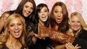 In the vibrant realm of Event Heroes, five extraordinary women stand united, their radiant smiles reflecting the joy and camaraderie that only they bring to life. Clad in their iconic costumes, they hold aloft a mighty brown boot — a symbol of triumph and adventure. Behind them, an ethereal backdrop of pink feathers dances with energy, setting the stage for an unforgettable celebration of heroism and delight. Together, they embody the spirit of fun and fellowship that defines every gathering in their legendary world. :The Event Heroes at Black Tie Productions