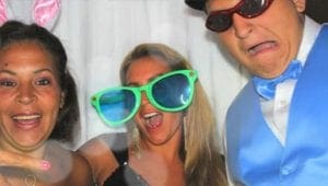 In the midst of an electrifying Michigan wedding, a trio of extraordinary individuals revel in vibrant disguise. The Enchantress of Carrots dazzles with her mystical bunny ears, channeling the playful spirit of boundless joy. Beside her stands the Emerald Visionary, her enormous green spectacles casting a charismatic aura over all who dare to gaze within them. Completing this dynamic assembly is Sir Dapper Blue, resplendent in his sapphire suit and commanding top hat, accented by crimson shades that radiate intrigue. Together, they create an iconic tableau—a scene tailor-made for legendary photo booth escapades. Against the backdrop of heart-pounding rhythms spun by masterful DJs, this gathering ignites imaginations and immortalizes memories at the celebrated event!. :The Event Heroes at Black Tie Productions