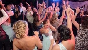 In the heart of the celebration, where jubilation meets destiny, a valiant league of dancers assembles on the gleaming dance floor. Each one clad in their semi-formal battle gear, they move with electrifying energy, lifted by an invisible force toward an apex of joy. They raise their hands to the heavens in synchronized triumph as vibrant beams of light bathe them in a kaleidoscope of colors—a beacon signaling that tonight belongs to legends. At the command center stands the Michigan wedding DJ, a maestro of momentum and guardian of grooves, expertly orchestrating an unstoppable rhythm that elevates this gathering into legendary status. This is not just a party; it’s an Odyssey led by Event Heroes themselves!. :The Event Heroes at Black Tie Productions