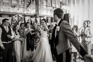 In the heart of a rustic barn, where bales of hay transform into seats and bunting waves like victory banners, the dynamic duo—bride and groom—take to the floor. They glide across the wooden battleground, their dance a symphony of love that captivates an audience of joyful witnesses. This magical moment, immortalized in timeless black and white, began its journey to legend status thanks to Black Tie Productions. With their prowess in DJ alchemy, they forged an atmosphere so electric it could rival any thunderstorm over Michigan skies! The celebration became nothing short of unforgettable—a supernova event bursting with joy and heroism on this day of extraordinary union!. :The Event Heroes at Black Tie Productions