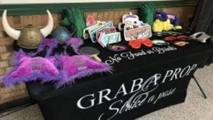 Behold, the legendary Prop Table, laden with whimsical disguises and enchanted tokens—hats of mystique, glasses that twinkle with mischief, and signs bearing proclamations of mirth. A mighty banner calls forth all who dare: Grab a Prop, Strike a Pose! Event Heroes descend upon this gathering with their unparalleled powers, casting radiant beams of event lighting to transform your revelry into an unforgettable odyssey. This spectacle is destined for every festivity or Michigan wedding DJ extravaganza!. :The Event Heroes at Black Tie Productions