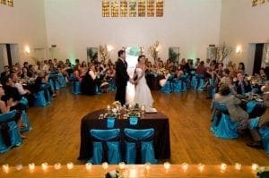 In a grand room illuminated by the dynamic brilliance of Black Tie Productions, our valiant bride and groom command the center stage, encircled by their loyal guests. Tables cloaked in majestic blue and accompanied by flickering candles form an enchanting backdrop. The scene is further amplified by superb event lighting, crafting a setting that befits only the most legendary Michigan wedding DJ adventure!. :The Event Heroes at Black Tie Productions