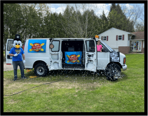 In the vibrant world of fun and festivities, a mighty white van, adorned with eye-catching cartoon graphics, stands triumphantly on the verdant grass. From it erupts a dazzling stream of bubbles that sparkle like stars in daylight. As the side door swings open, revealing a dynamic portal to thrilling adventures, two guardians stand proudly: an animated penguin mascot and a cheerful ally clad in a vivid pink shirt. Together, they herald the City Wide Rides experience—a beacon of joy and excitement. These Event Heroes are masters of merriment! With their unparalleled powers, they transform ordinary moments into extraordinary memories while offering swift price quotes for any occasion. Their mission is clear: bring joy to all who seek it!. :The Event Heroes at Black Tie Productions