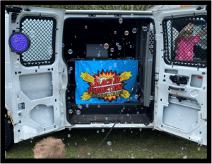 In the bustling metropolis of celebration, a vibrant van emblazoned with the emblem of Slacktive Productions: Your Event Heroes roars onto the scene, bursting with whimsy and wonder. Bubbles dance through the air like tiny guardians of joy, weaving enchantment around all who gather. Within this mobile fortress of fun, glimpses reveal a young sidekick and an enigmatic figure clad in pink—ambassadors of mirth and memory. Together, they champion unforgettable experiences for anyone seeking photo booth adventures or epic Michigan wedding DJ performances. With these heroes on your side, every event becomes legendary!. :The Event Heroes at Black Tie Productions