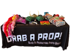 In the heart of the bustling gala, a mighty table stands, laden with an arsenal of whimsical props ready to transform any guest into a hero of their own making. Feather boas flutter like capes caught in a gust; a Viking helmet gleams with battle-ready pride; foam fists await those who wish to channel their inner powerhouses; and sunglasses conceal secret identities with effortless cool. Among these treasures, signs boldly declare: Grab a Prop! Black Tie Productions Photo Booths! Enhance your epic event with the brilliance of professional lighting or summon the Event Heroes for an instant price quote that will elevate your celebration to legendary status. :The Event Heroes at Black Tie Productions