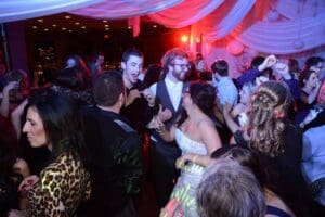 In the heart of the bustling metropolis, a dynamic squad of electrifying individuals unleashes their epic dance moves at a vibrant indoor gathering. The atmosphere crackles with energy as kaleidoscopic beams of colorful event lighting cut through the air, transforming the venue into a dazzling realm of celebration. Stationed like a secret lair at one corner is an exhilarating photo booth rental, where partygoers strike legendary poses and capture their heroic camaraderie in frames of infinite fun. Its not just any party; its a high-octane convergence where joy and vibrancy meet in an unforgettable showdown!. :The Event Heroes at Black Tie Productions