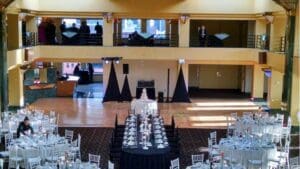 Amidst the gleaming opulence of the scene, Black Tie Productions orchestrated a spectacle worthy of legend, transforming a grand hall into a bastion of elegance. Round tables stood like sentinels of grace around a commanding rectangular table showcasing an exquisite cake that promised sweet triumph. Above, in their own lofty realm, guests mingled with sophistication and poise, basking in an ambiance crafted by true artisans of celebration. :The Event Heroes at Black Tie Productions