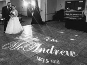 Under the dazzling lights of their wedding day, the powerful duo known as Bret & Ella McAndrew rises heroically onto the dance floor. Their names, Bret & Ella McAndrew May 5, 2018, beam beneath them like a legendary emblem, marking this union as one for the ages. In the shadows stands their trusty ally—an illustrious Michigan DJ booth—capturing every enchanted moment with unwavering precision and ensuring that every beat echoes through history. This day is theirs to protect and cherish forever!. :The Event Heroes at Black Tie Productions