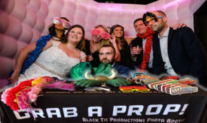 In the dazzling realm of celebration, a spirited squad assembles, their ensemble punctuated by vivid props in a kaleidoscope photo booth, courtesy of the legendary Black Tie Productions. The backdrop of this electrifying chapter is magnified by awe-inspiring event lighting, illuminating the scene like arcs of energy from a supernova. Nearby, an arsenal of whimsical props stands ready, inviting these heroes to unleash waves of creativity and conquer the forces of ordinary with their boundless imagination!. :The Event Heroes at Black Tie Productions