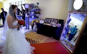 Amidst the grandeur of an elegant ceremony, our heroine stands poised on a radiant red carpet, her wedding attire a shimmering symbol of purity and strength. Her eyes lock onto a grand mirror framed by beams of brilliant light, illuminating her path with promise. Beyond this reflective portal, the masterminds at Black Tie Productions have engineered an extraordinary table brimming with fantastical props, amplifying the magic in this enchanted realm where dreams unfold. :The Event Heroes at Black Tie Productions