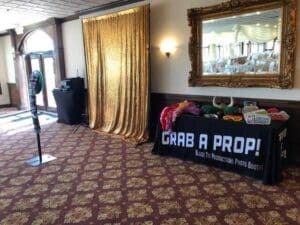 In the dazzling realm of event planning, behold the magnificent Photo Booth of Power! Transform any gathering into an epic spectacle with its shimmering golden backdrop that radiates heroism and style. Fear not, for alongside stands the legendary Grab a Prop! table, overflowing with whimsical artifacts—hats and glasses—that arm our guests with fun and laughter. Unleash the full force of this experience by summoning professional event lighting to elevate the ambiance into an unforgettable marvel. Unite these elements, and watch as they create a legendary atmosphere worthy of any superhero saga!. :The Event Heroes at Black Tie Productions