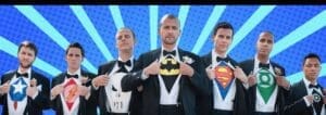 In a scene that pulses with the energy of a comic book showdown, seven extraordinary figures stand resolute against a vivid blue backdrop. Each man, clad in the immaculate guise of a tailored suit, unveils the emblem of heroism that beats beneath his exterior—icons such as Captain Americas mighty shield, Flashs electrifying bolt, Punishers fierce skull, Batmans cunning silhouette, Superman’s legendary S, and Green Lantern’s radiant ring. Their presence is accentuated by the vibrant sunburst design behind them and bathed in the dramatic event lighting orchestrated by Black Tie Productions. Together they form an ensemble of justice ready to leap into action at a moments notice. :The Event Heroes at Black Tie Productions