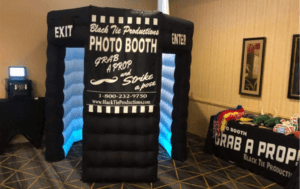 In the grand hall of celebration, where memories await their immortalization, stands a colossus of captured magic—the Inflatable Photo Booth! Adorned with the emblem of Black Tie Productions, this mighty structure graces the room with its presence. Beside it lies a trove of delightful props, ready to assist in crafting legendary moments. Perfect for any Michigan wedding or event, this heroic setup ensures that every memory is preserved in glorious fashion!. :The Event Heroes at Black Tie Productions