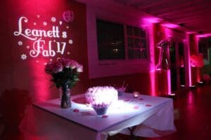 Behold, the legendary celebration lair where elegance meets extraordinary! A mesmerizing table stands as the centerpiece, adorned with resplendent pink floral creations and a bounty of delectable treats fit for heroes. Ambient pink lighting casts its enchanting glow across the realm, transforming it into a haven of wonder. In dazzling letters on the wall reads Leanetts Fab 17, an emblem of new beginnings and ultimate style! Black Tie Productions swoops in with their unparalleled mastery of sound and spectacle, crafting an unforgettable musical odyssey that ensures guests embark on an evening theyll remember forever! Prepare for party prowess like never before!. :The Event Heroes at Black Tie Productions
