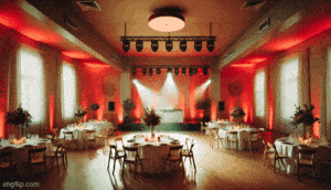 Behold the majestic Event Hall of Elegance, where round tables don pristine white capes and stand adorned with magnificent centerpiece vases, all illuminated by a glow as warm as a heros heart. A grand stage emerges from the shadows, cloaked in draped curtains and bathed in spotlight glory, ready to embrace your triumphant celebration. Supercharge your experience with the dynamic duo of a photo booth rental or Michigan wedding DJ—guaranteeing an evening of legendary status. Instant price quotes are available faster than a speeding bullet!. :The Event Heroes at Black Tie Productions