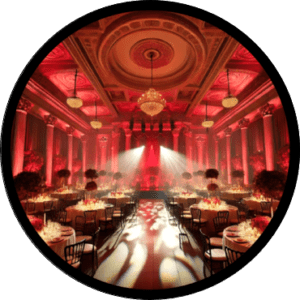 Behold the majestic ballroom, draped in a heroic shade of crimson that casts an aura of grandeur across the space. The ceiling above is a marvel, intricately adorned with designs as complex and captivating as the most thrilling saga. Beneath this ornate canopy stand valiant round tables, poised in perfect formation. Their companions, the noble black chairs, await steadfastly for guests to gather for an epic event worthy of legends. :The Event Heroes at Black Tie Productions